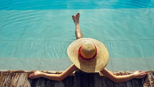 A person relaxing by a poolside with a wooden deck. - Aequora Lanzarote Suites (Tías)