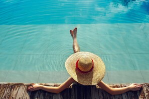 A person relaxing by a poolside with a wooden deck. - Aequora Lanzarote Suites (Tías)