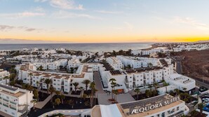 A coastal hotel complex with multiple buildings, palm trees, and a beach in the background. - Aequora Lanzarote Suites (Tías)