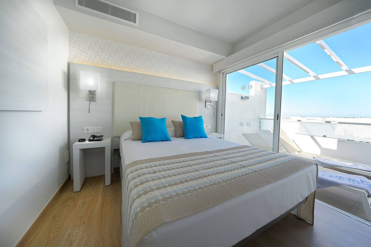 Habitación de hotel moderna con una cama grande, una mesita de noche, un escritorio y un balcón con vistas.