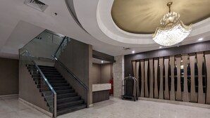 Un hall d’entrée moderne avec un sol en marbre, un escalier, un lustre et un comptoir d’accueil.