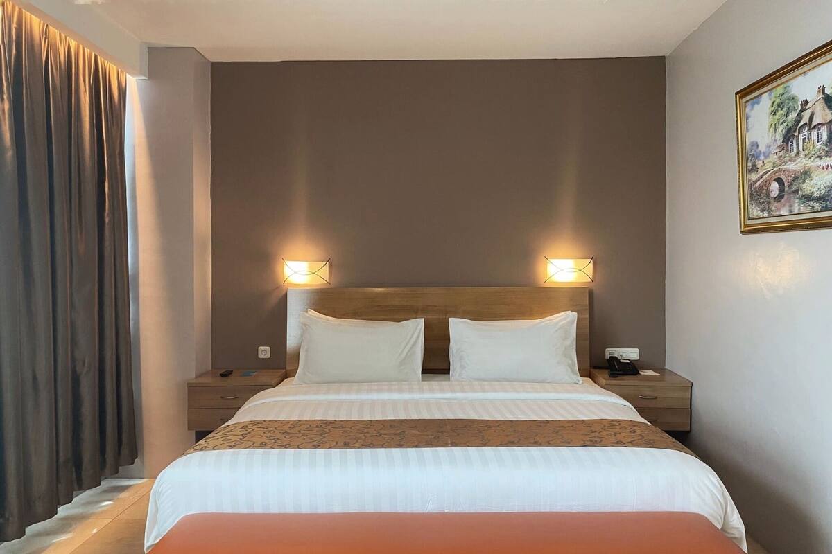 A hotel room with a large bed, two bedside tables, a bench, and a painting on the wall.