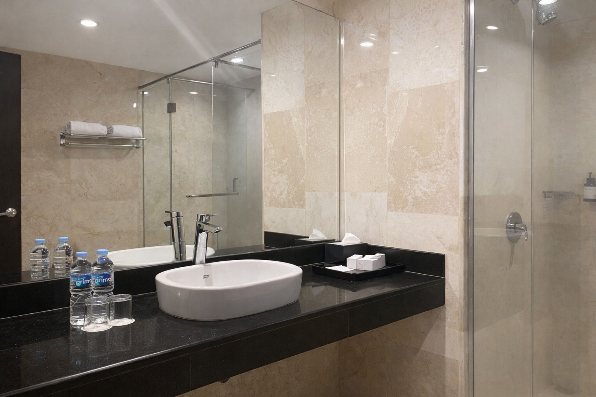 A modern bathroom with a large mirror, a white sink, and a glass-enclosed shower.