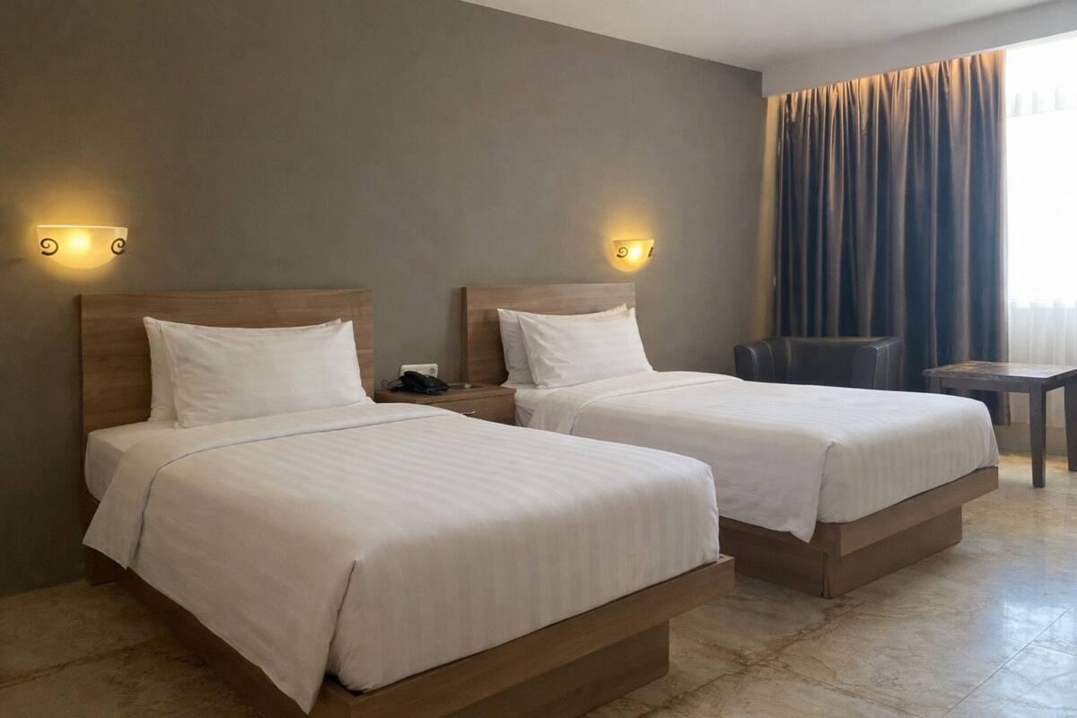 Two single beds with wooden headboards, bedside tables, and wall-mounted light fixtures in a hotel room.