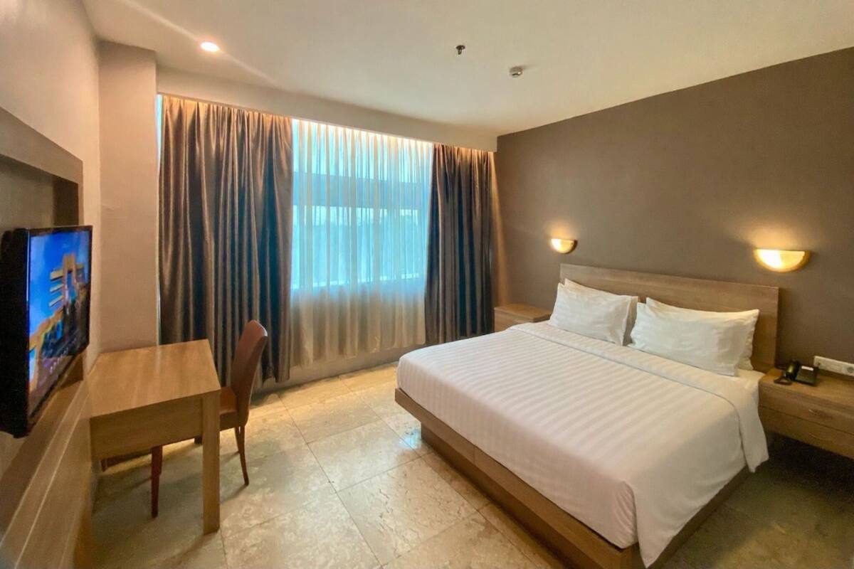 A hotel room with a bed, a desk, a chair, a television, and curtains.