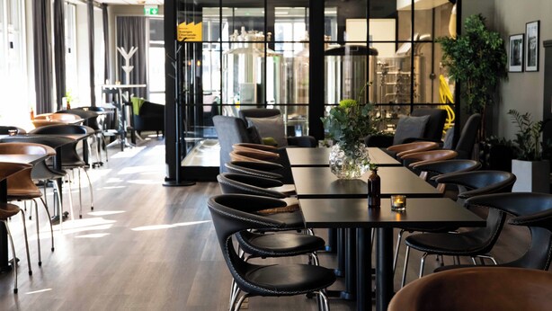 Un restaurante moderno con sillas y mesas de cuero negro, ventanas amplias y decoración de estilo industrial.