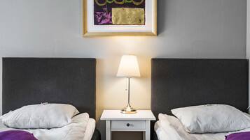 Una habitación de hotel con dos camas, una mesita de noche con lámpara y un cuadro enmarcado en la pared.