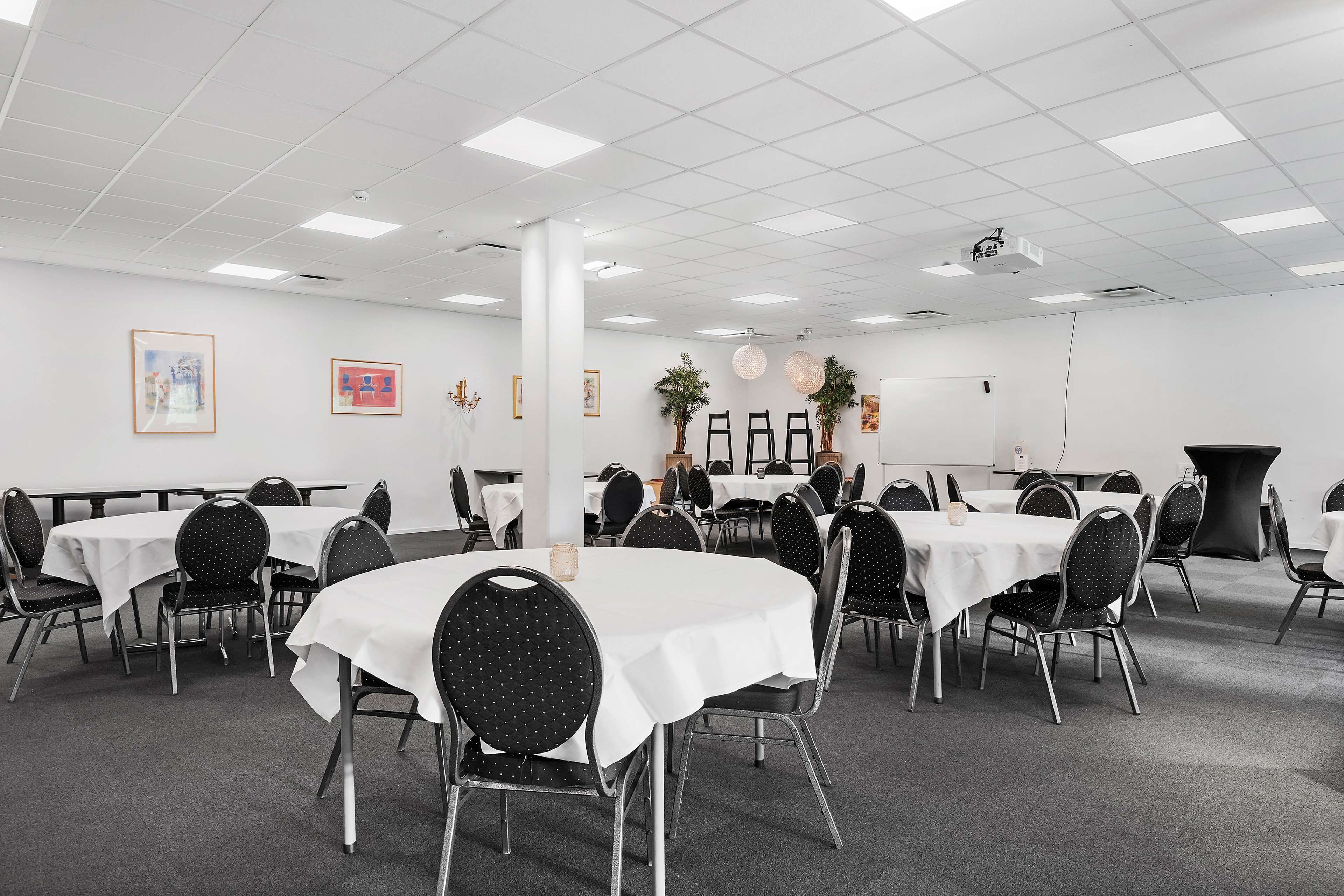 Une salle de conférence avec plusieurs tables rondes, des chaises noires et des nappes blanches.