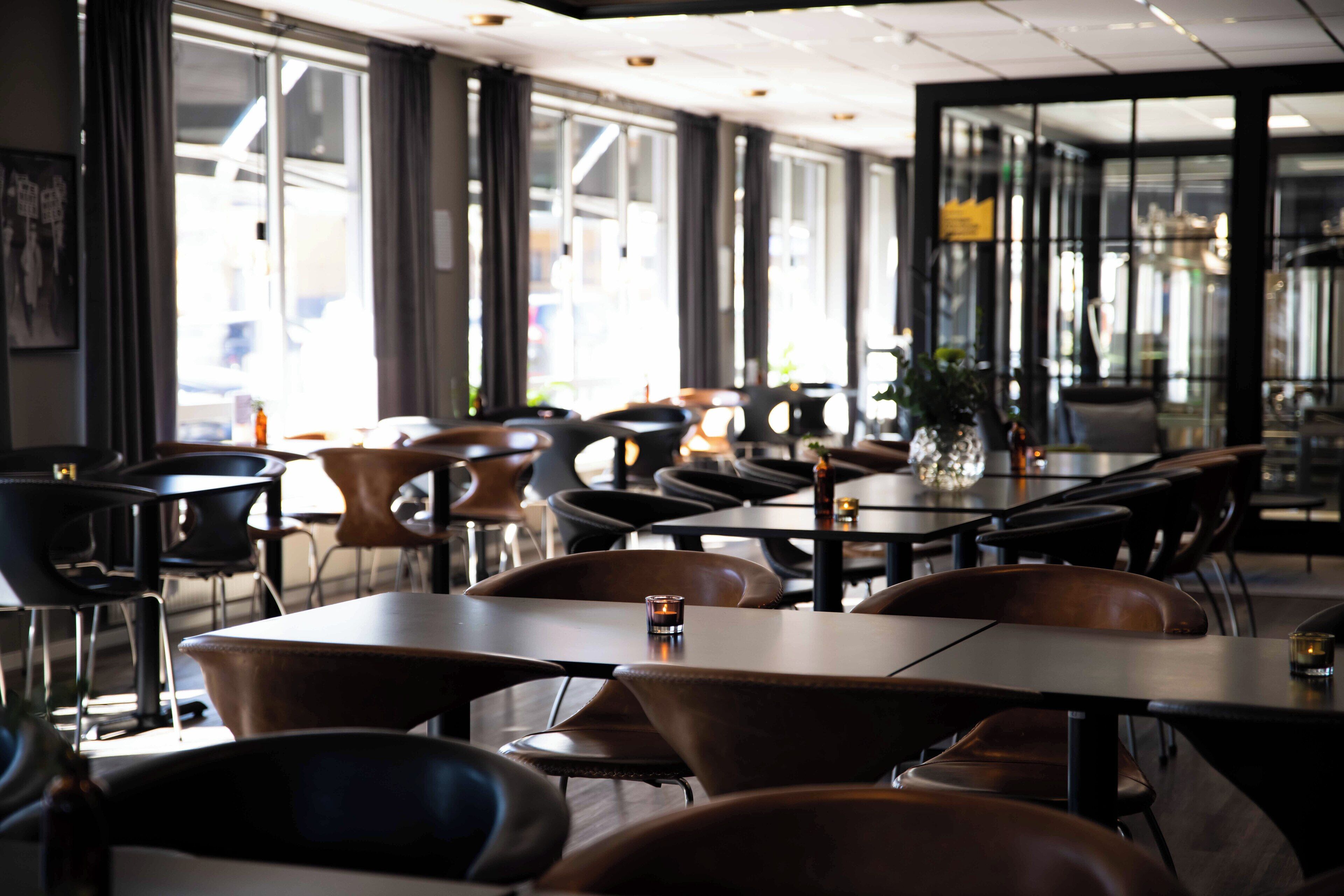 A modern restaurant with a mix of dark and light wood tables and chairs, large windows, and a clean, contemporary interior design.