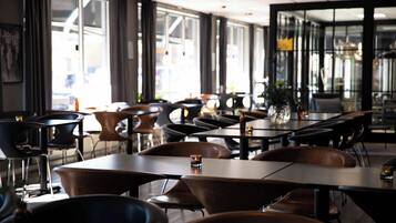 A modern restaurant with a mix of dark and light wood tables and chairs, large windows, and a clean, contemporary interior design.