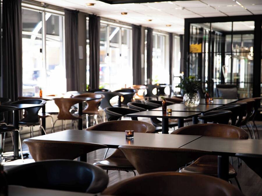 A modern restaurant with a mix of dark and light wood tables and chairs, large windows, and a clean, contemporary interior design.