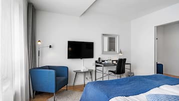 A modern hotel room with a large bed, a desk with a chair, a television, and a small table with a lamp.