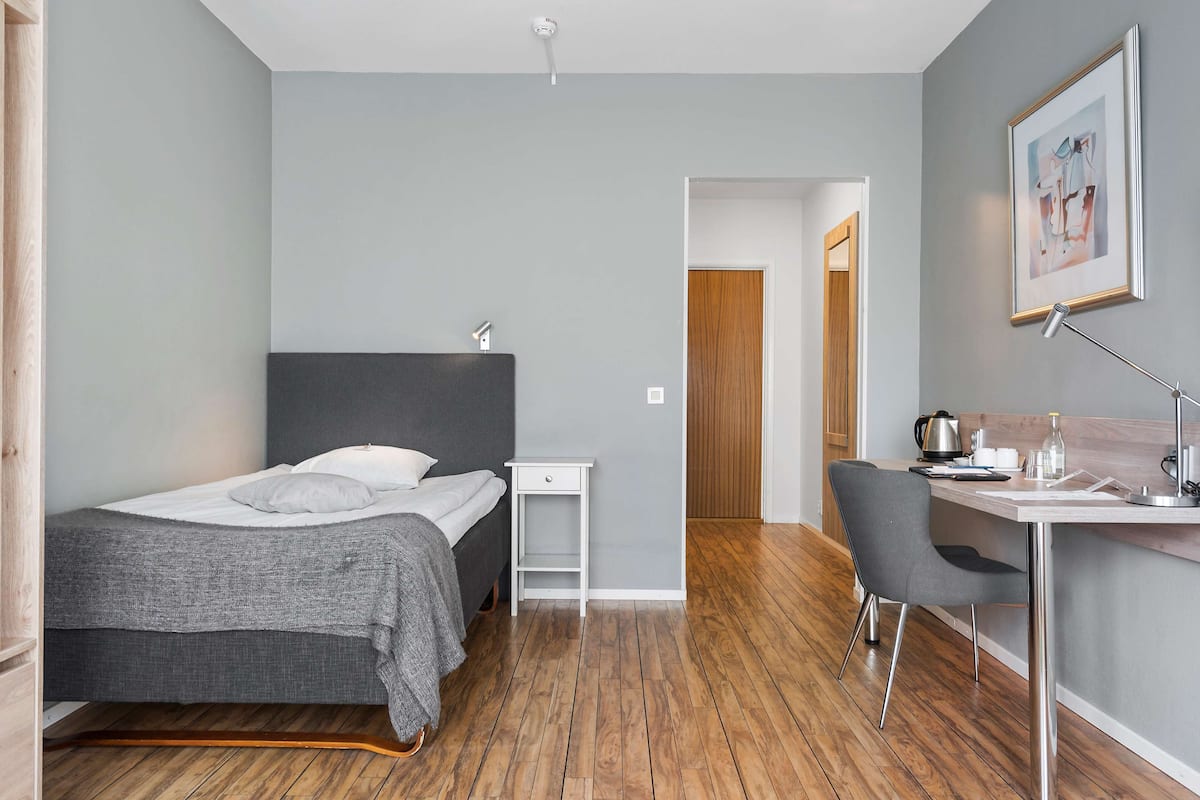 A modern bedroom with a bed, bedside table, desk, chair, and a framed picture on the wall.
