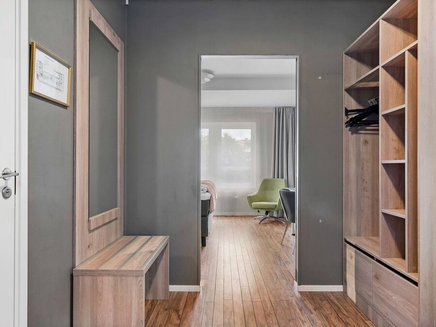 A hallway with a wooden bench, a green chair, and a wooden wardrobe with shelves.