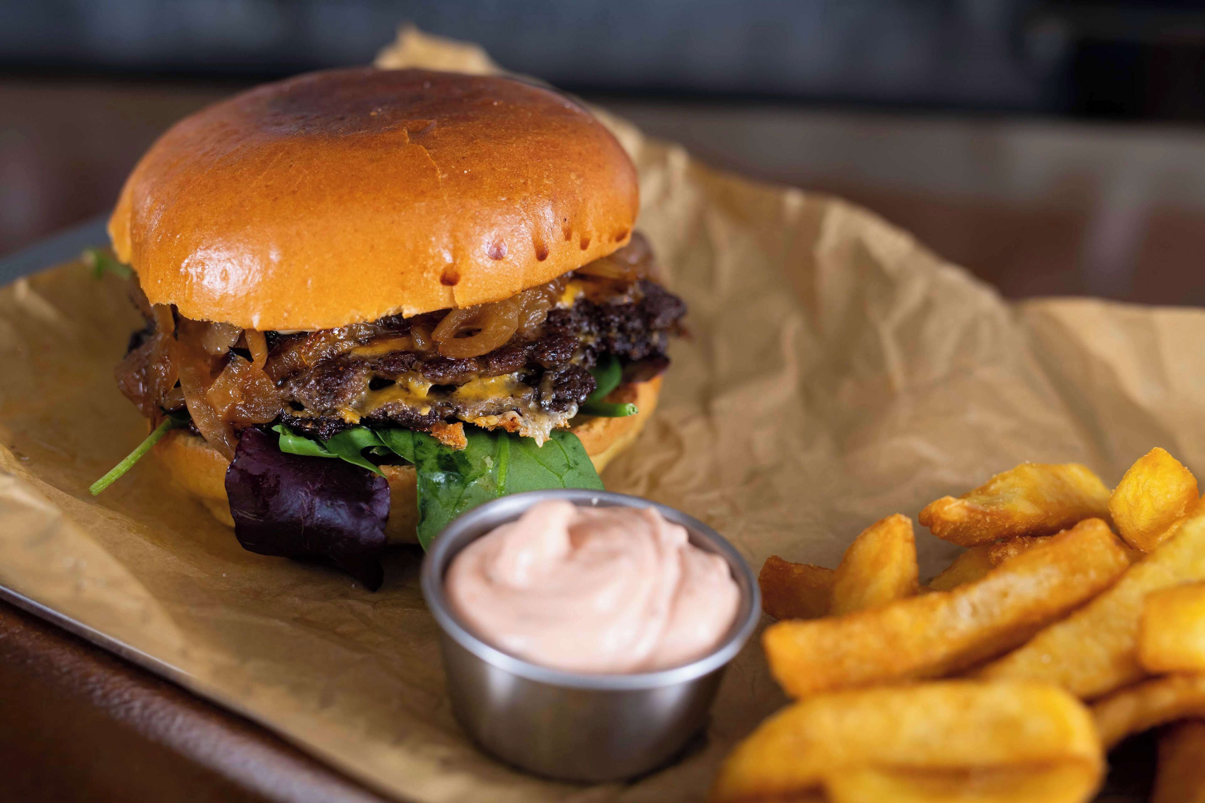 A burger with fries and a dipping sauce on a paper-lined tray.