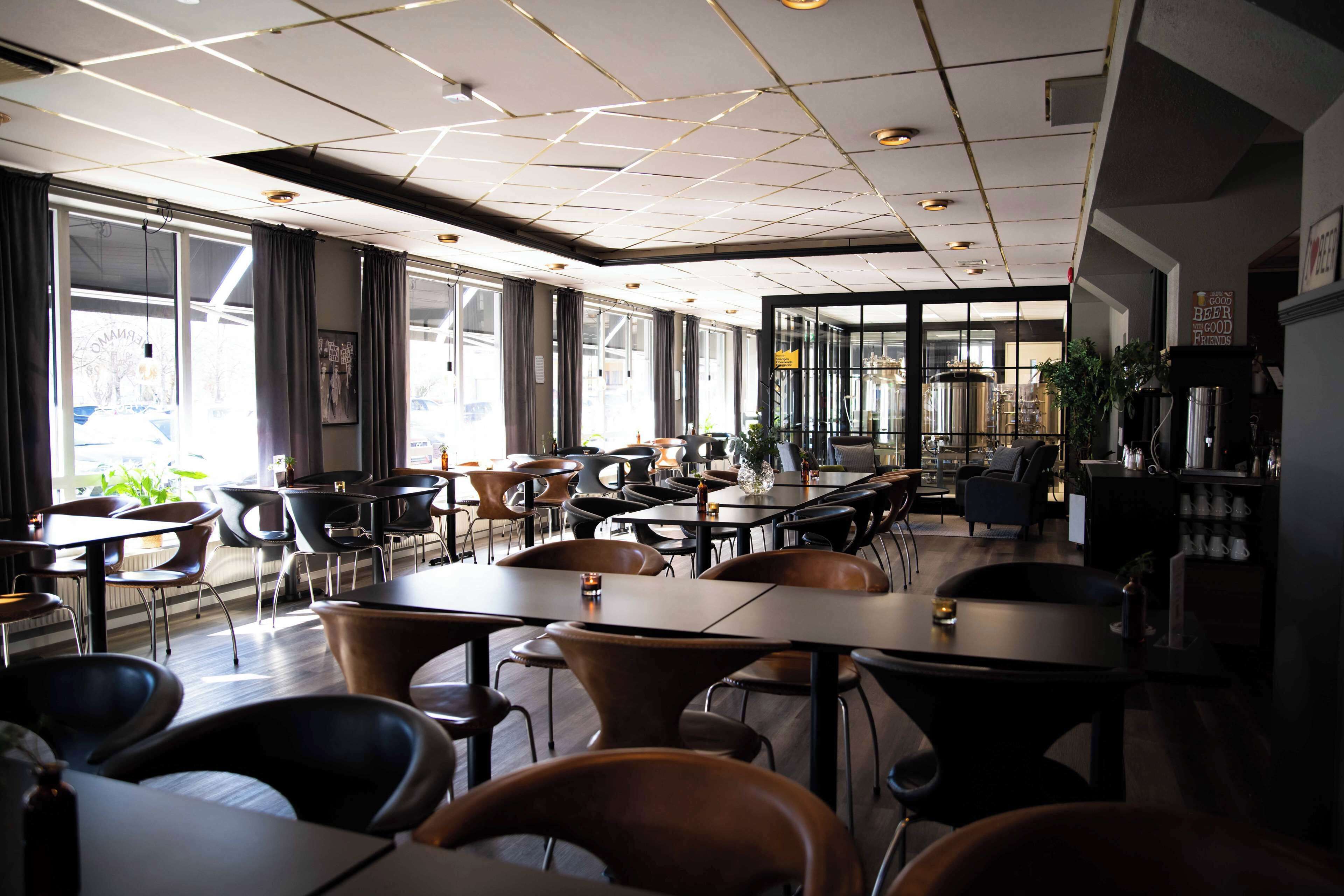 Un restaurante moderno con una variedad de opciones de asiento, como mesas y cabinas, y ventanas amplias que ofrecen vistas al exterior.