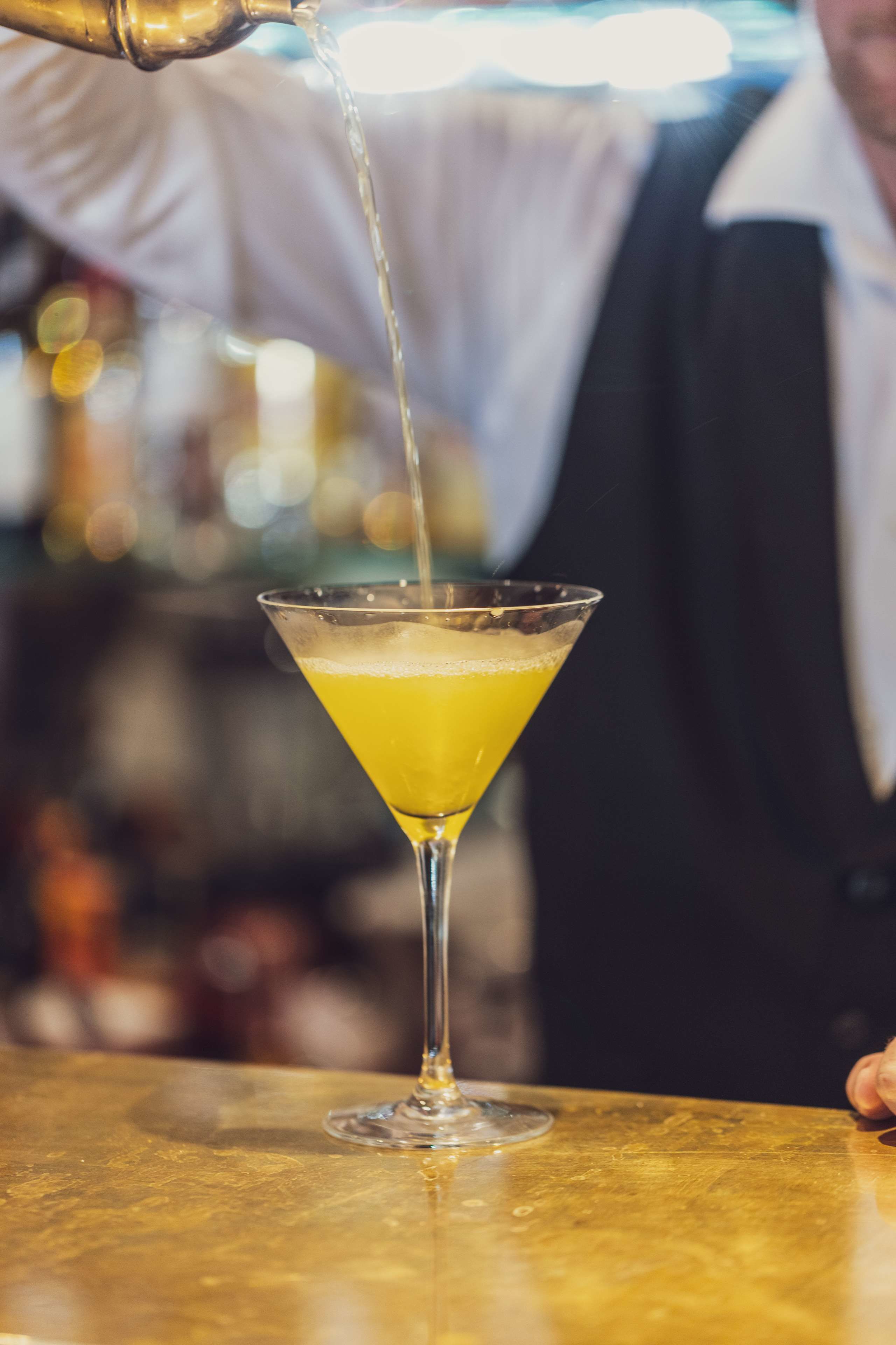 A bartender pouring a yellow drink into a martini glass.