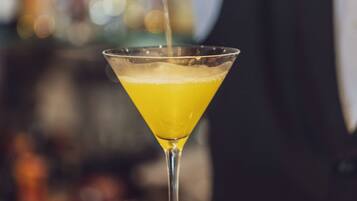 A bartender pouring a yellow drink into a martini glass.