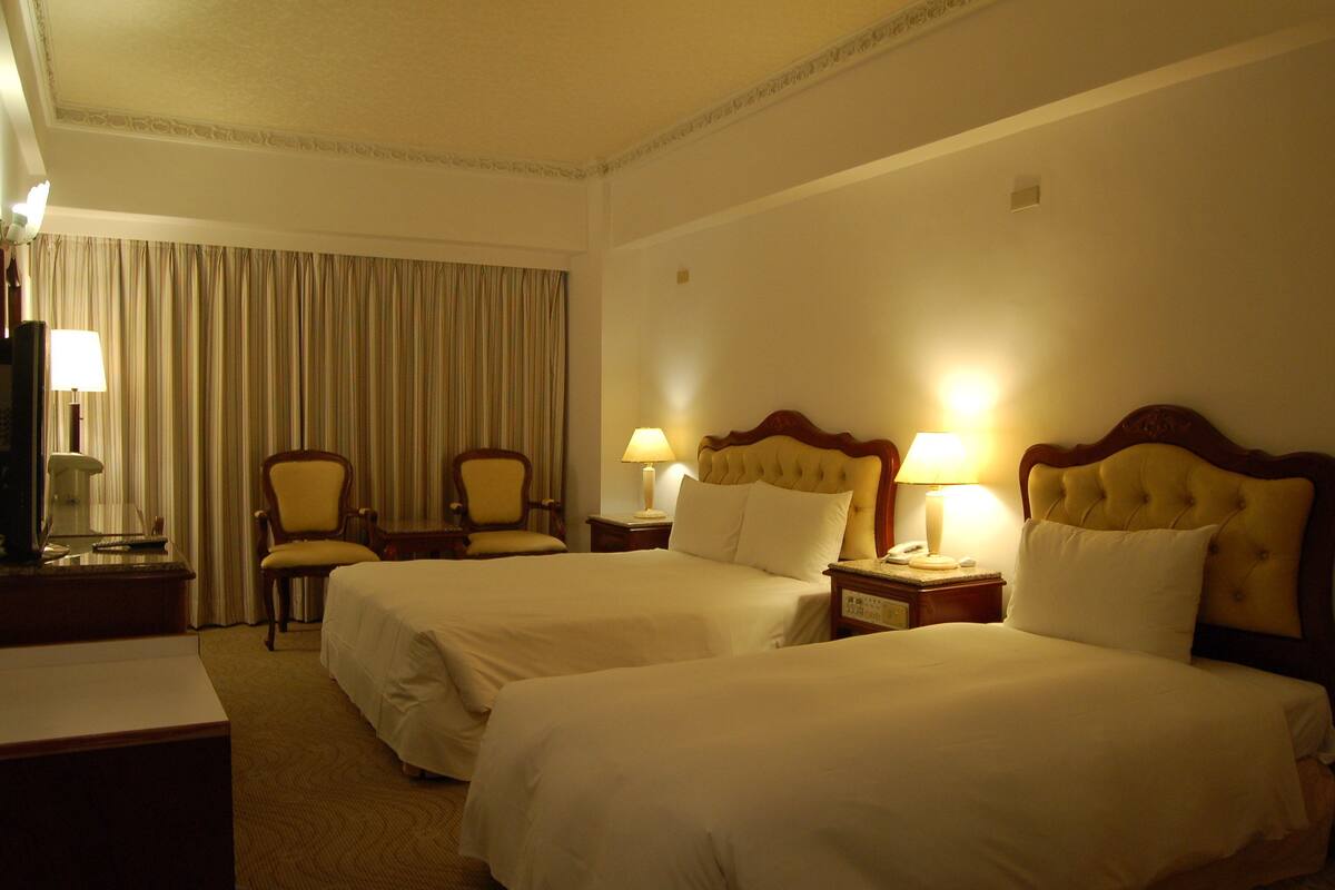 Habitación de hotel con dos camas, un escritorio, una silla y una lámpara.