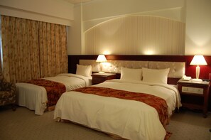 A hotel room with two beds, a headboard with a curved design, a nightstand with a lamp, and a patterned curtain. - Hua Tong Hotel (Hualien City)