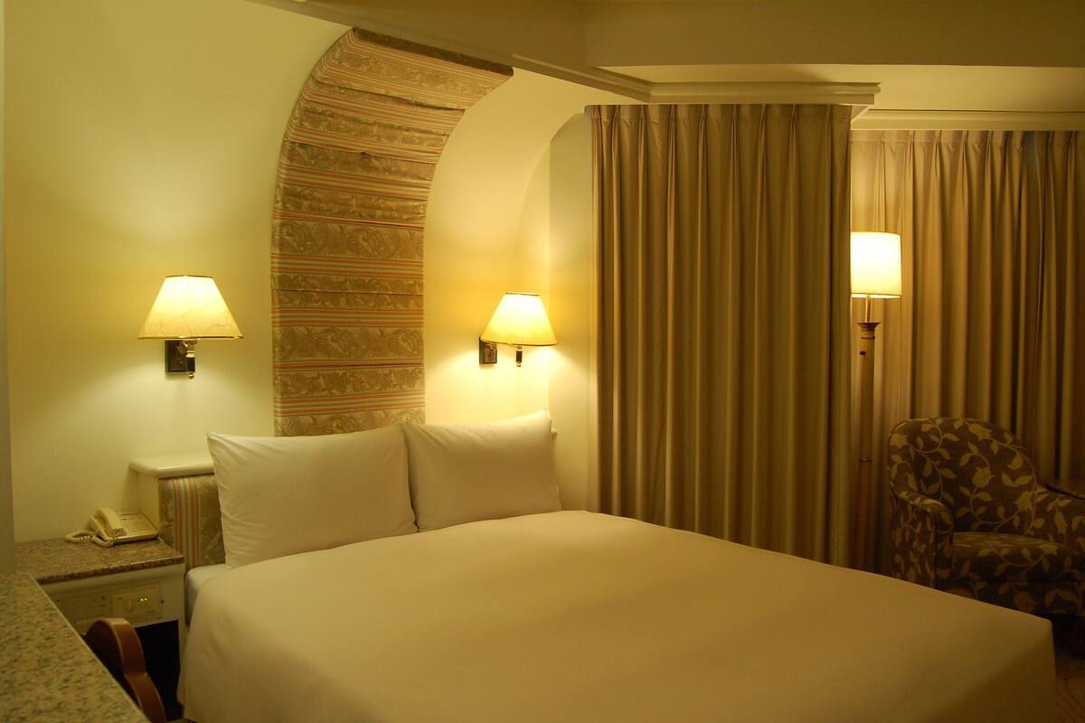 Una habitación de hotel con una cama grande, dos lámparas de noche, una silla y un teléfono en la mesita de noche.