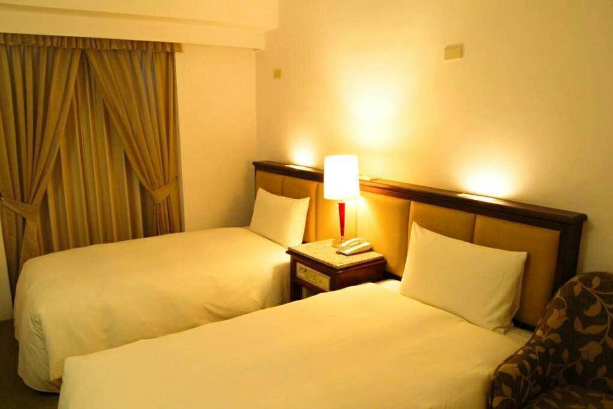 Una habitación de hotel con dos camas, una mesita de noche con lámpara y una silla.