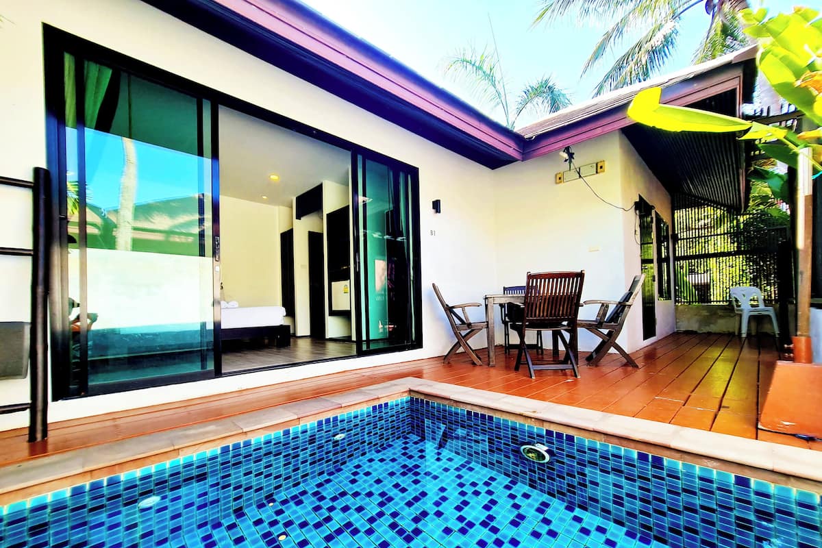 A modern pool area with a tiled floor, a wooden deck, and a glass-enclosed room with a bed.
