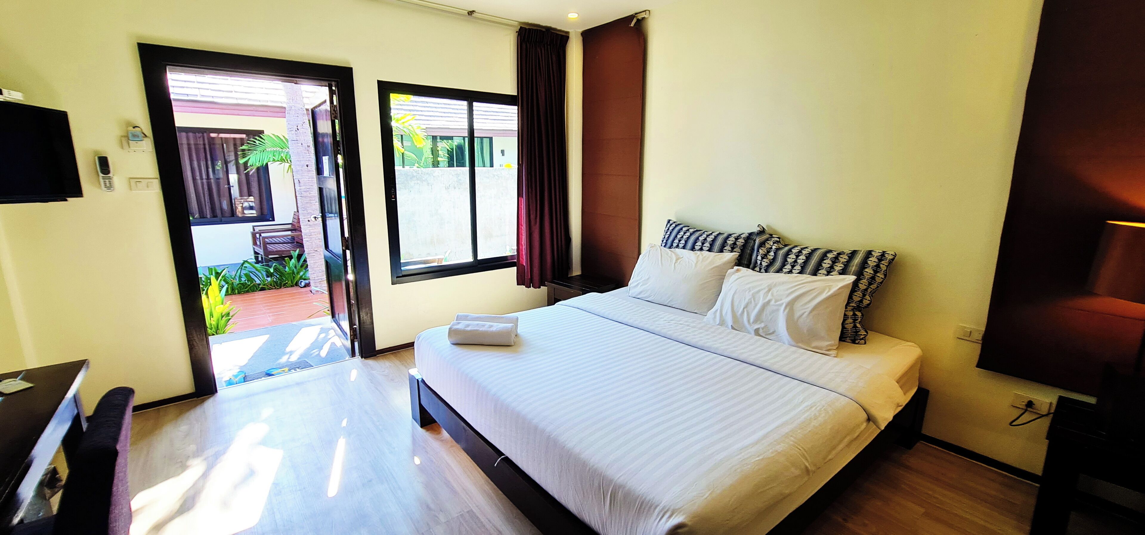 Habitación de hotel con cama, escritorio, silla, televisor y ventana con cortinas.