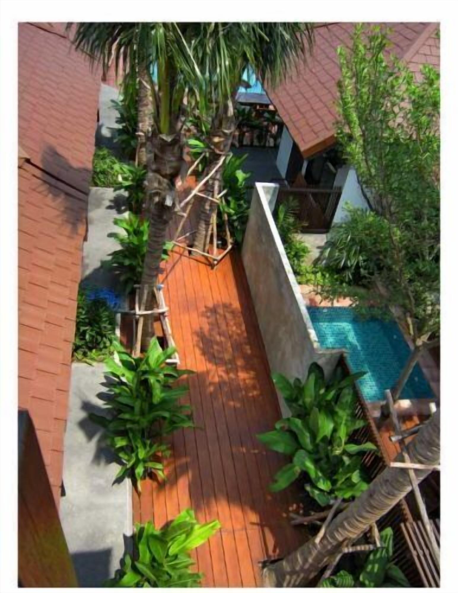A wooden deck with a pool, surrounded by lush greenery and a brick wall.