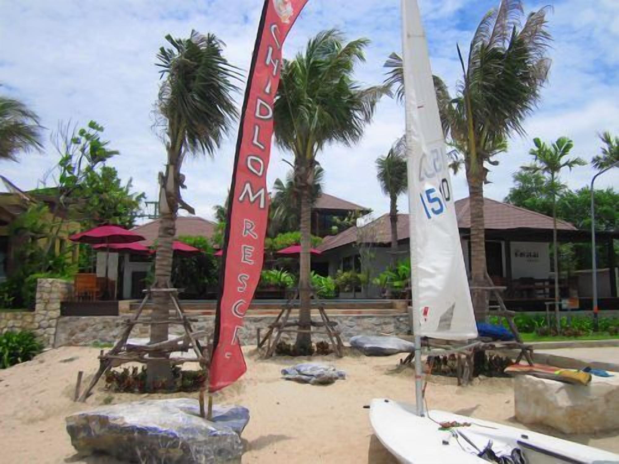 A beach area with a sailboat, a red flag, and palm trees.