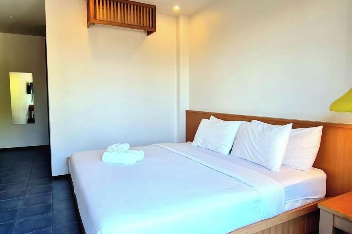 A neatly made bed with white linens and pillows, a wooden headboard, and a bedside table with a lamp.