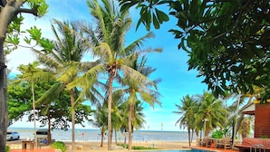 Un área de piscina con terraza de madera, palmeras y vistas a la playa.