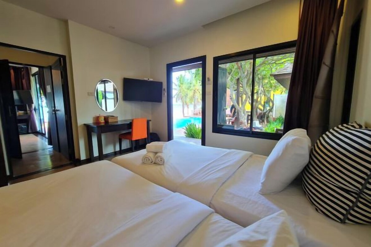 A hotel room with a large bed, a desk with a chair, a television, and a view of a pool and palm trees.