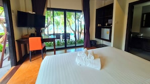 Habitación de hotel con cama, escritorio, silla, televisor y vistas a una piscina y palmeras.