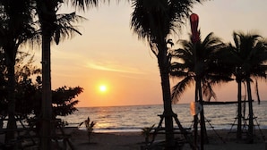 Escena de playa con palmeras y un atardecer sobre el océano.