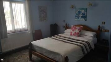 Un dormitorio con cama, un radiador, una ventana con cortinas, un reloj de pared y un cuadro.
