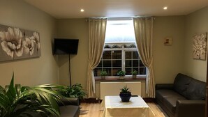A living room with a sofa, a coffee table, a TV, and a window with curtains. - The Balkan Lodge Oxford  (Oxford)
