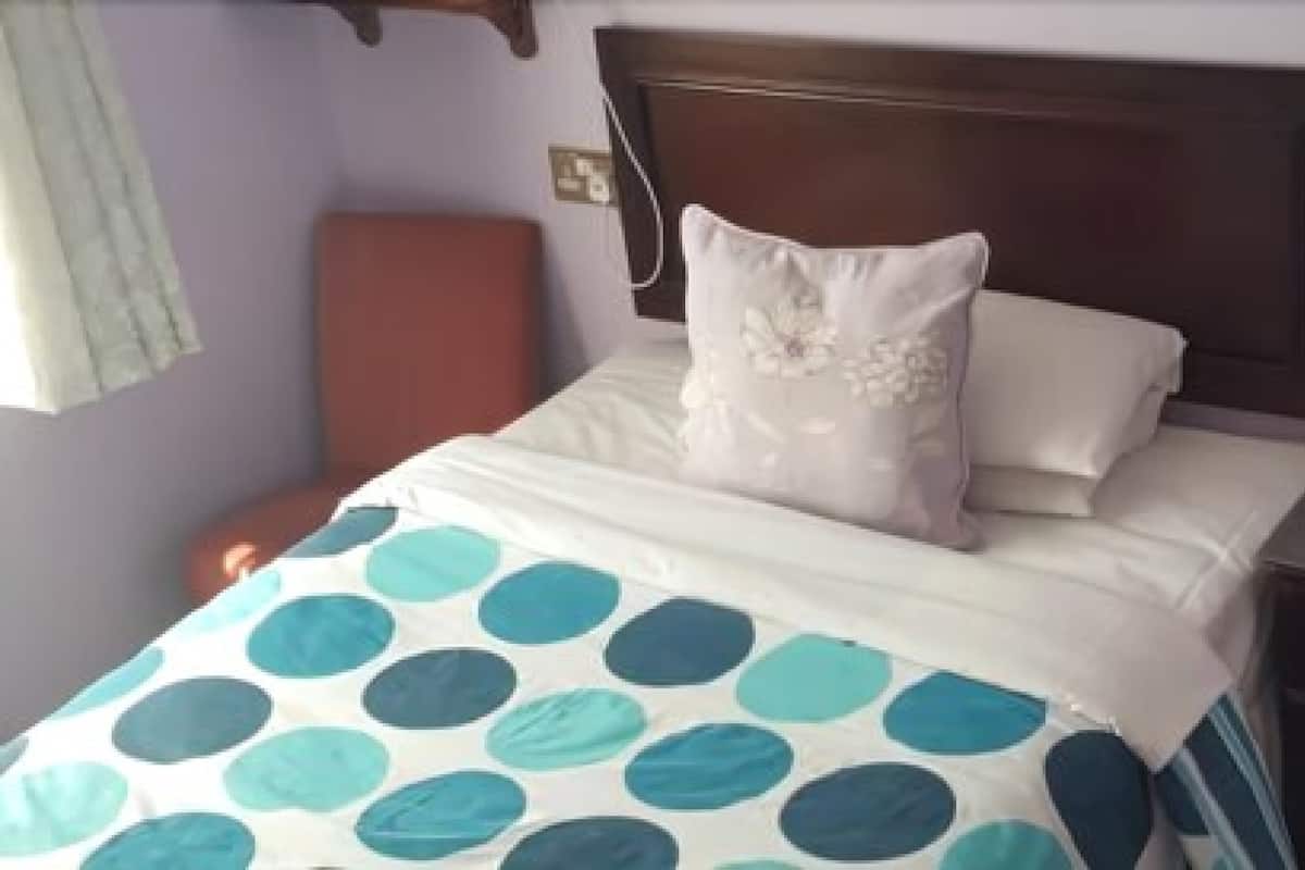 A hotel room with a bed, a nightstand with a phone, and a wall clock.