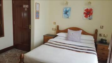 A neatly made bed with a striped bedspread and two pillows, a wooden nightstand with a lamp, and a door with a sign.