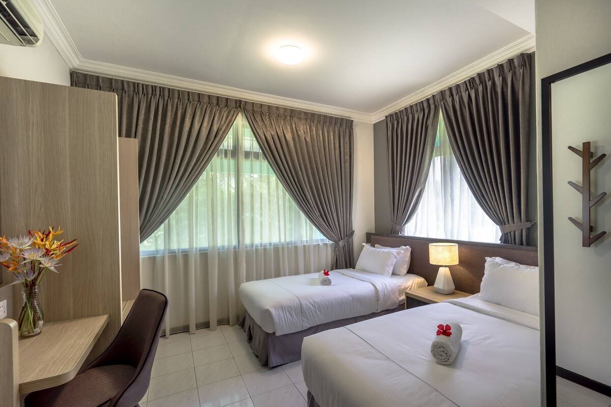 Habitación de hotel con dos camas, un escritorio, una silla, una lámpara y un florero con flores.