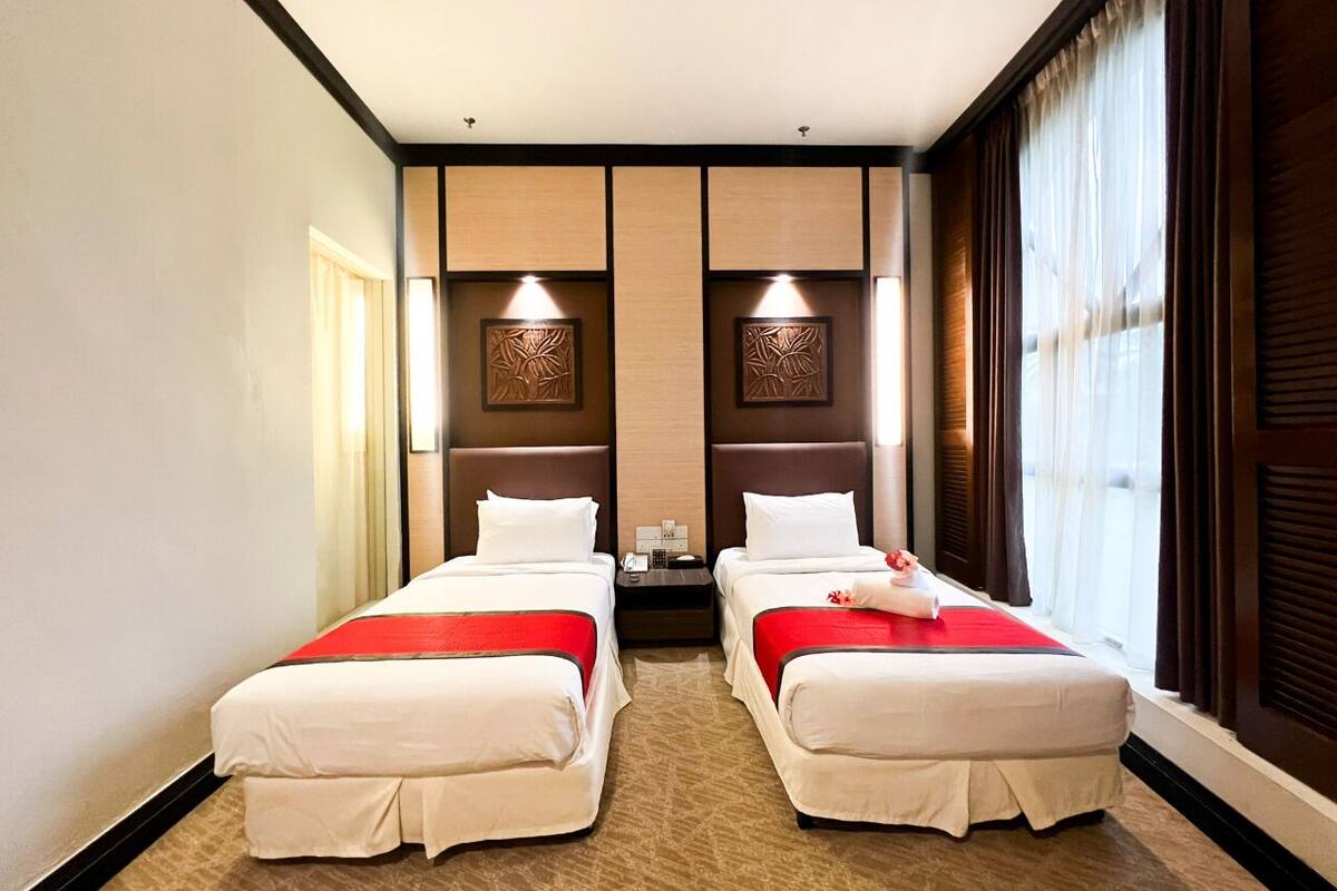 Una habitación de hotel con dos camas, una mesita de noche y un ventanal con cortinas.
