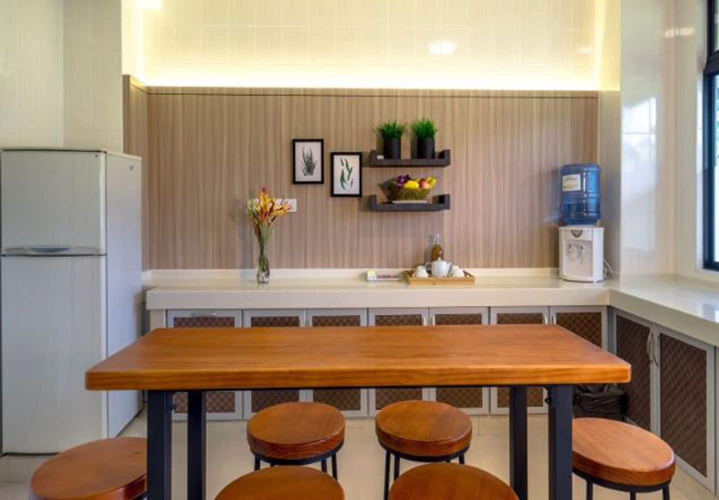 A modern kitchen with a wooden table and four stools, a refrigerator, and decorative items on the wall.