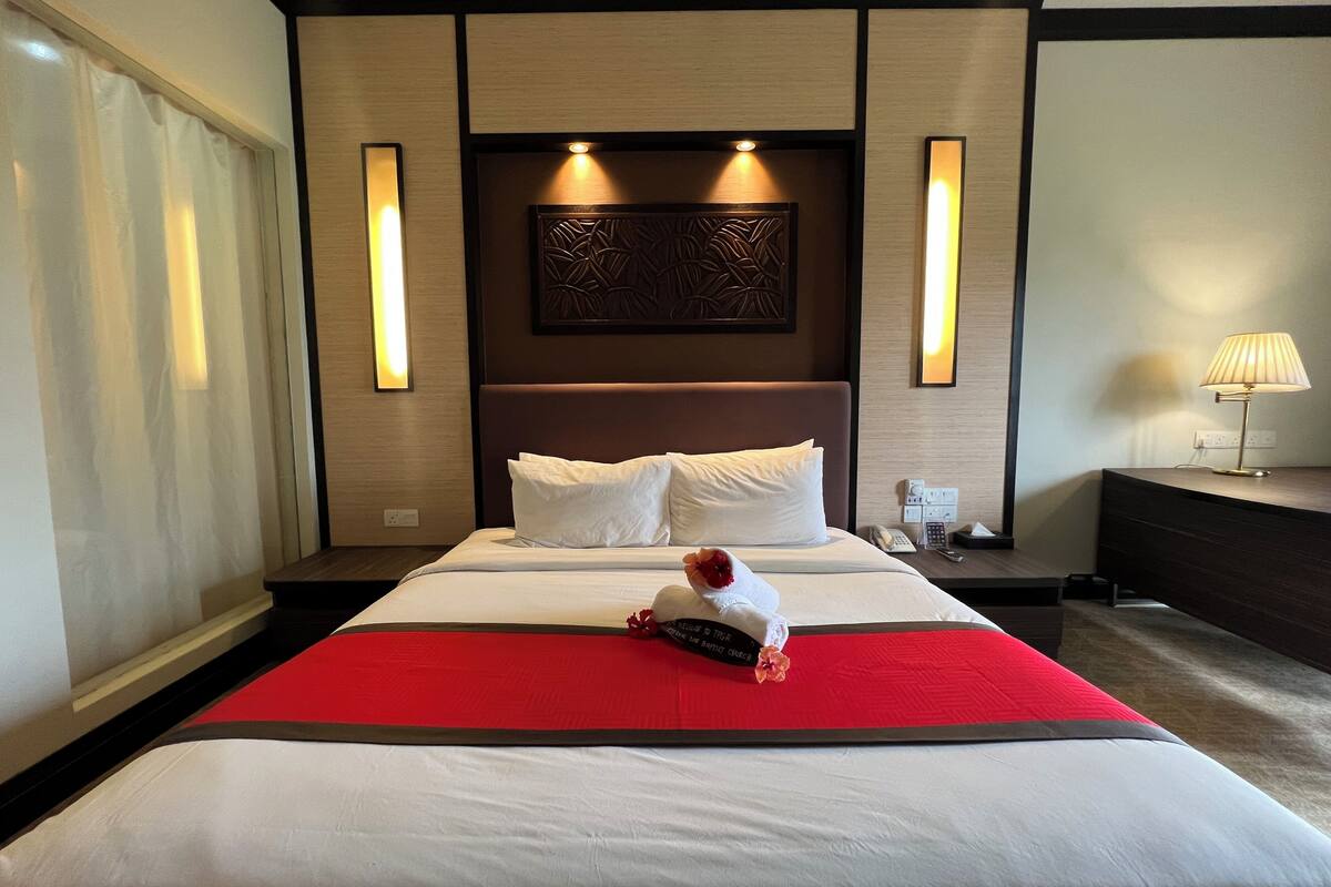 Habitación de hotel con una cama grande, lámparas de noche, una mesita de noche y un panel decorativo en la pared.