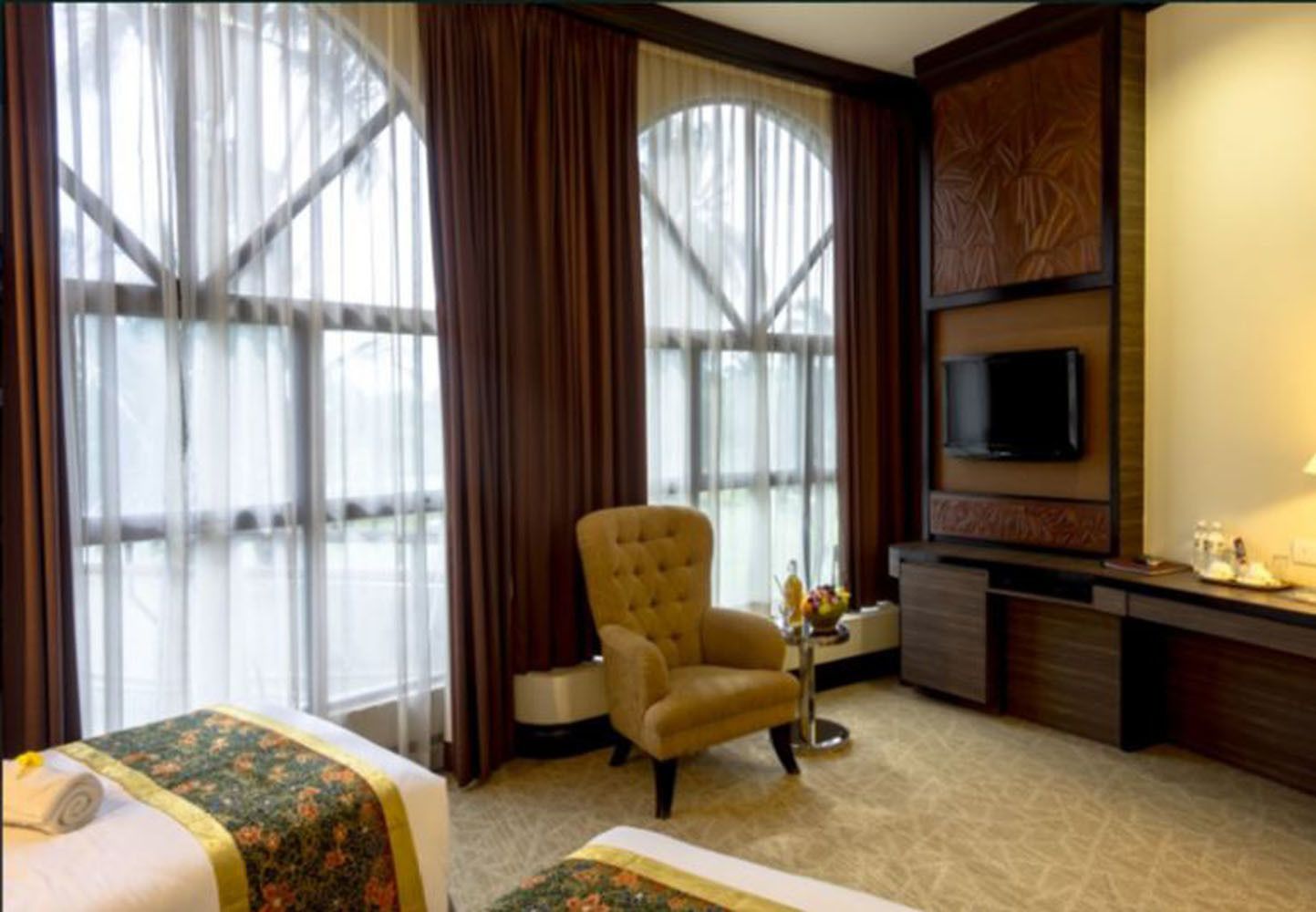 Habitación de hotel con un ventanal grande, un televisor en la pared, una silla y un escritorio con una lámpara.