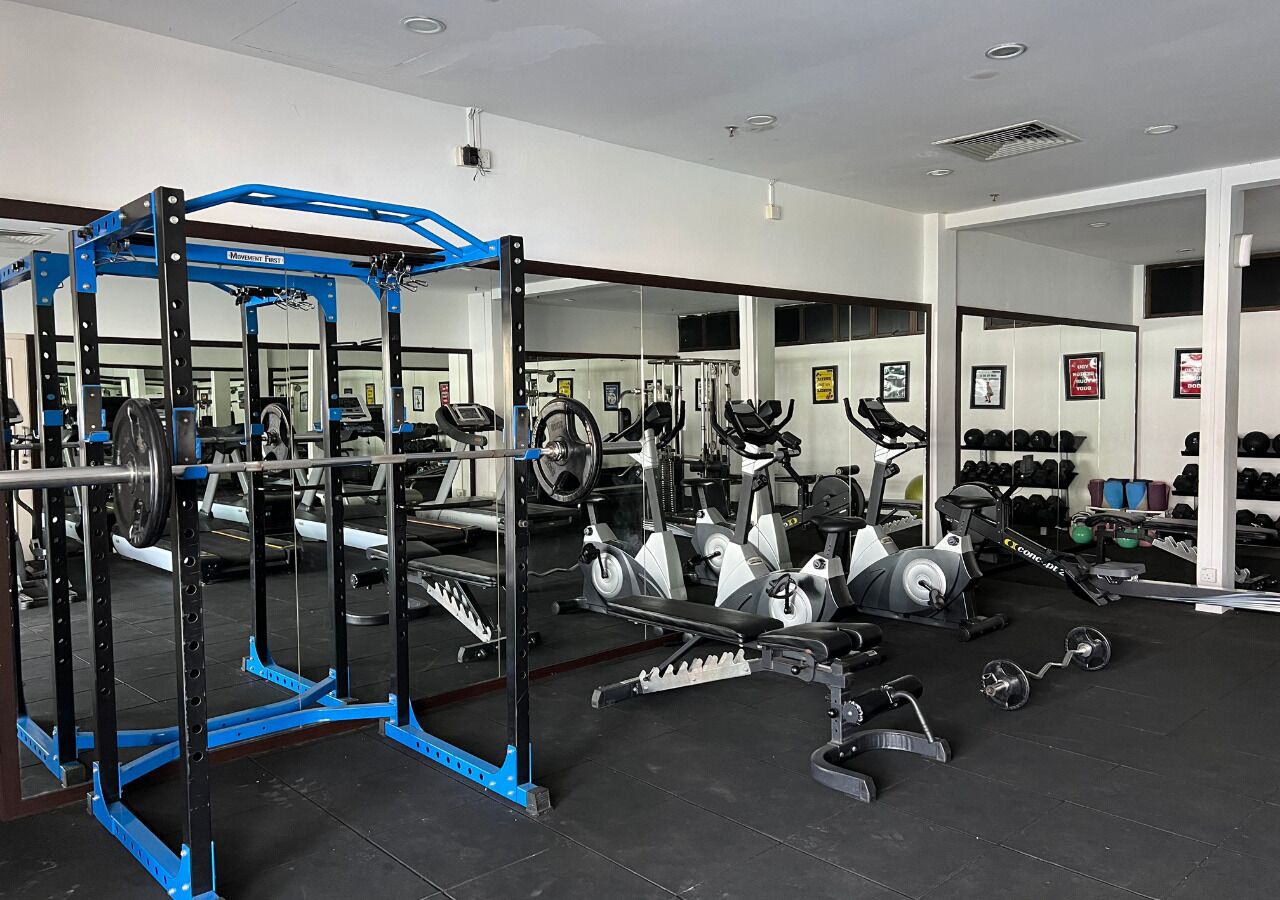 Un gimnasio con diversos equipos de ejercicio, incluyendo una estación de levantamiento de pesas azul, cintas de correr y bicicletas estáticas.