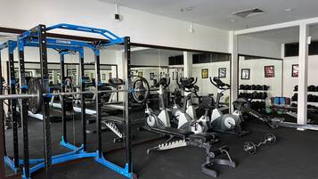Un gimnasio con diversos equipos de ejercicio, incluyendo una estación de levantamiento de pesas azul, cintas de correr y bicicletas estáticas.
