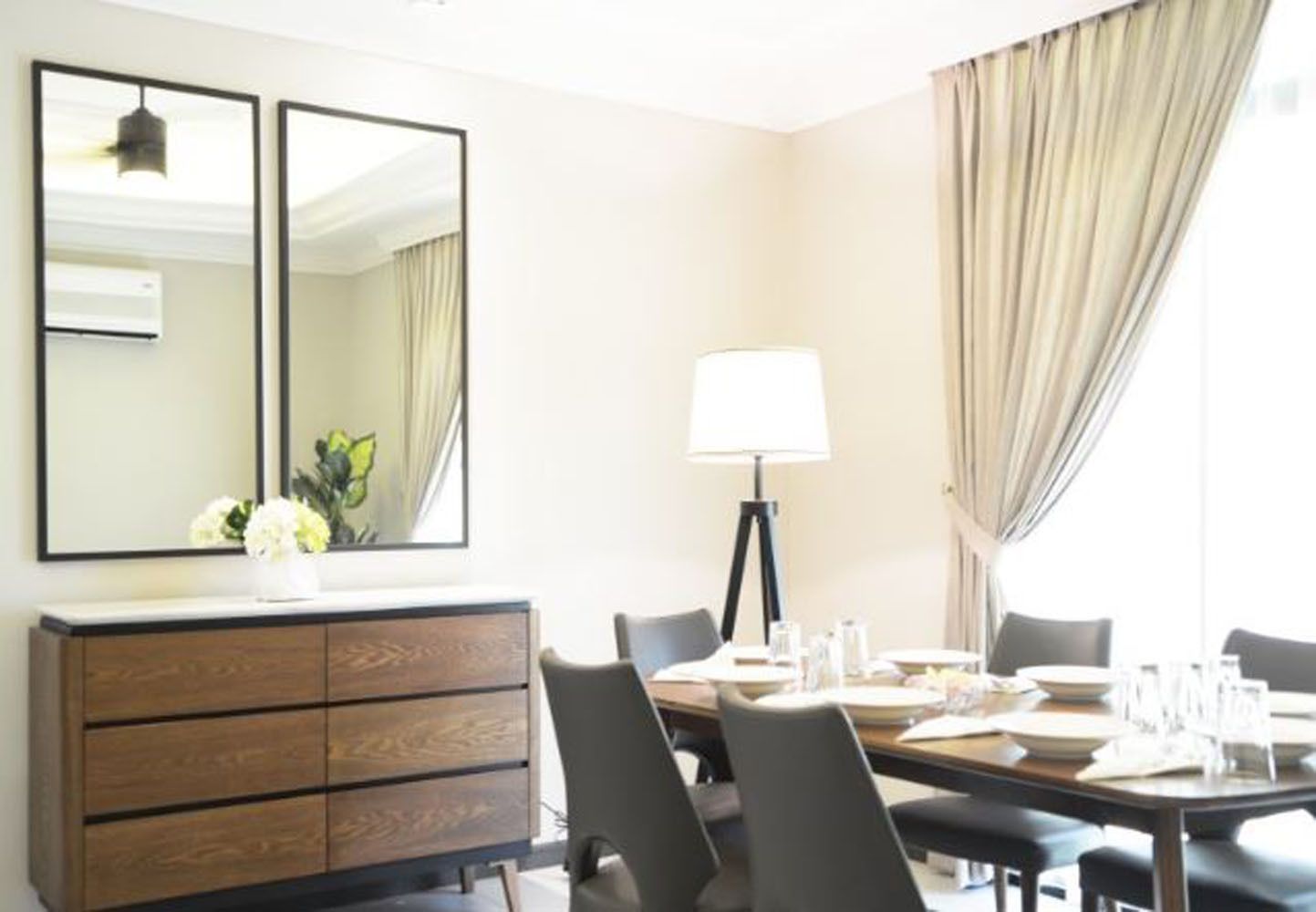 A hotel room with a dining area, a wooden dresser, a lamp, and a large mirror.