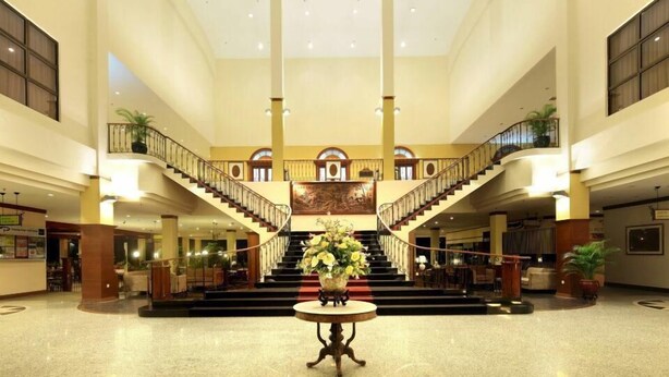 A spacious lobby with a central staircase, a reception desk, and a decorative vase with flowers. - Tanjong Puteri Golf Resort - Malaysia (Pasir Gudang)