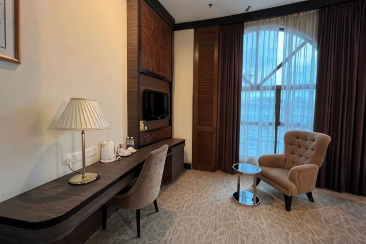 Habitación de hotel con escritorio, silla, televisión y vistas amplias a través de grandes ventanales.