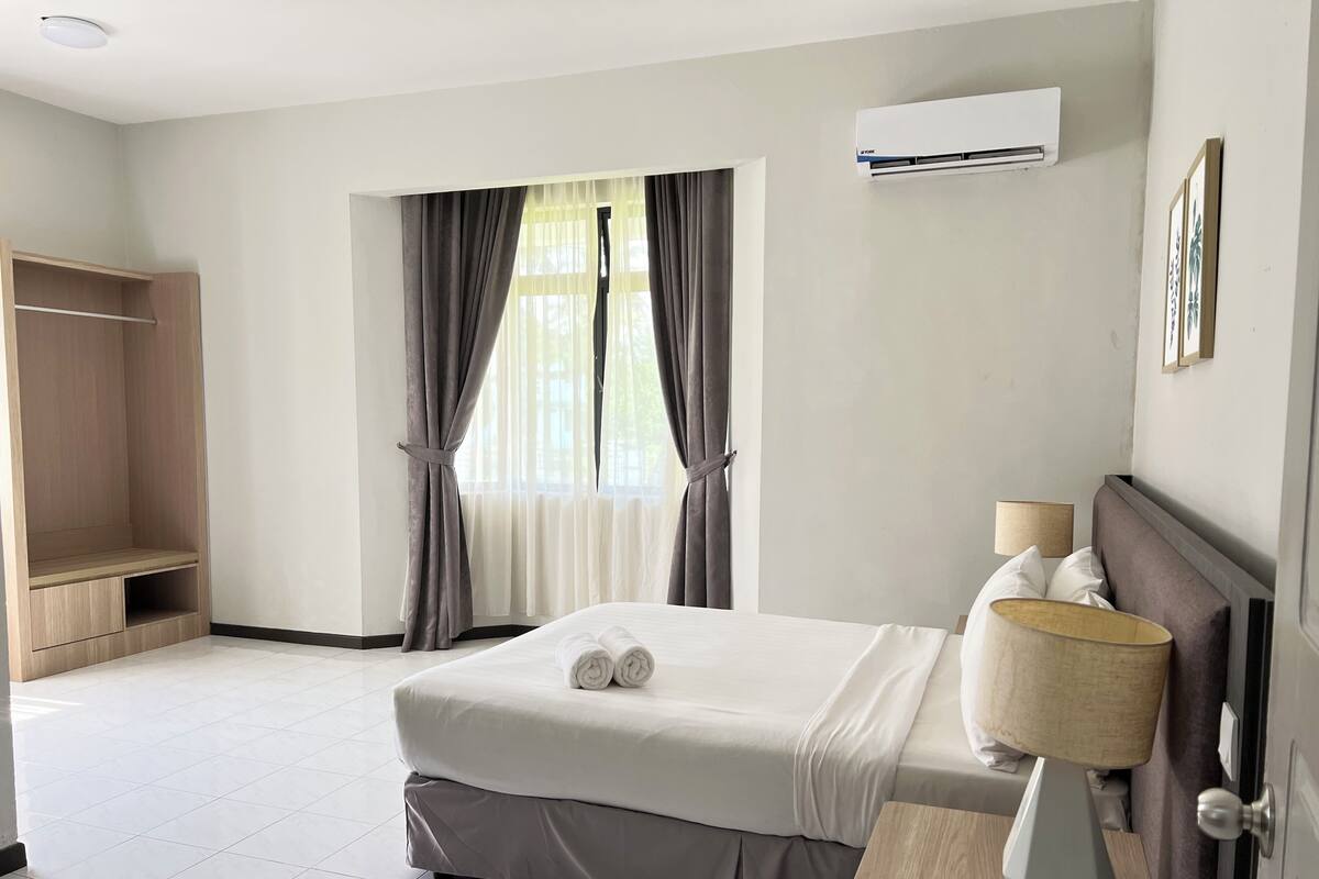 Habitación de hotel con cama, mesita de noche con lámpara, armario y aire acondicionado.